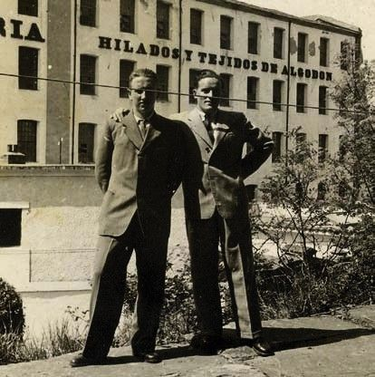 Dos hombres no identificados posan ante la fábrica de Oria; en la fachada se lee Hilados y Tejidos de Algodón.